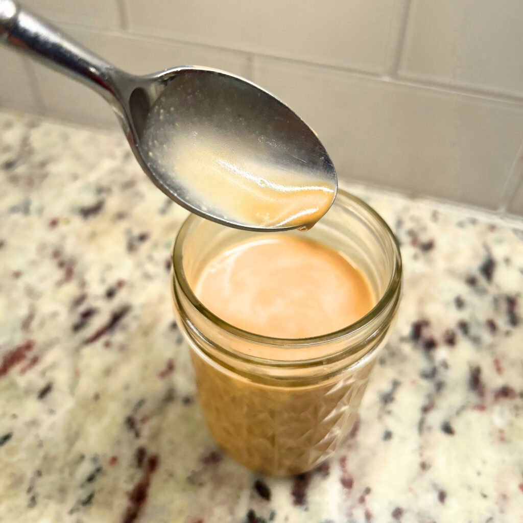 balsamic vinaigrette dressing in mason jar with spoon hoovering over jar with dressing into jar.