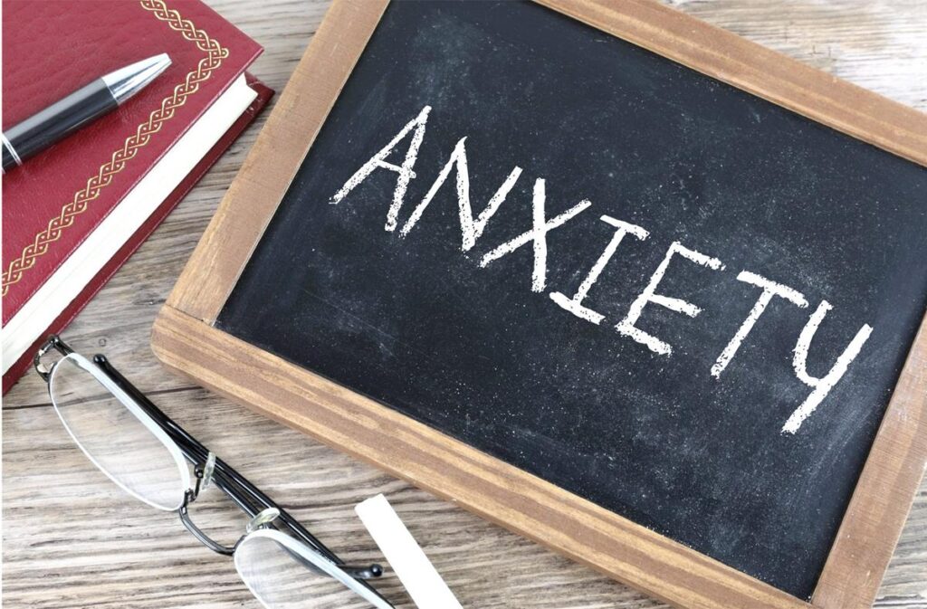 anxiety written on a small chalkboard with a book, pen, glasses, chalk on a table